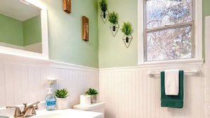 A bathroom with a white vanity, a toilet, a window with a view, and a blue rug. - The Big Blue Mesmerizing Mirror Home- 6 Mins to DT (Jacksonville)