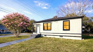 A single-story house with a front porch, a small front yard, and a tree with pink flowers. - The Big Blue Mesmerizing Mirror Home- 6 Mins to DT (Jacksonville)