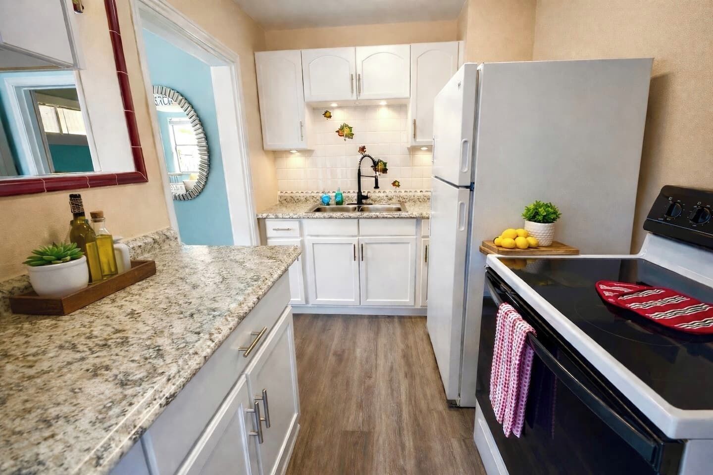 A kitchen with white cabinets, a granite countertop, a stainless steel refrigerator, and a black stove.