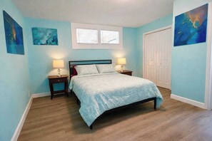 Une chambre à coucher avec un lit, deux tables de chevet, une fenêtre et des œuvres d’art accrochées aux murs.