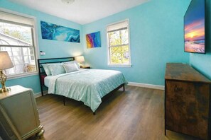 Quarto com cama, duas janelas, cômoda e obras de arte nas paredes.
