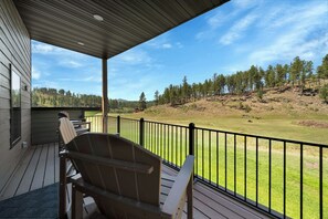 A covered deck with chairs, a view of a grassy field, and a forested hillside. - Experience the vibe of Hill City, South Dakota (Hill  City)