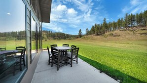 Eine Terrasse mit rundem Tisch und Stühlen, einem Glastisch sowie Blick auf eine Wiese und Bäume.