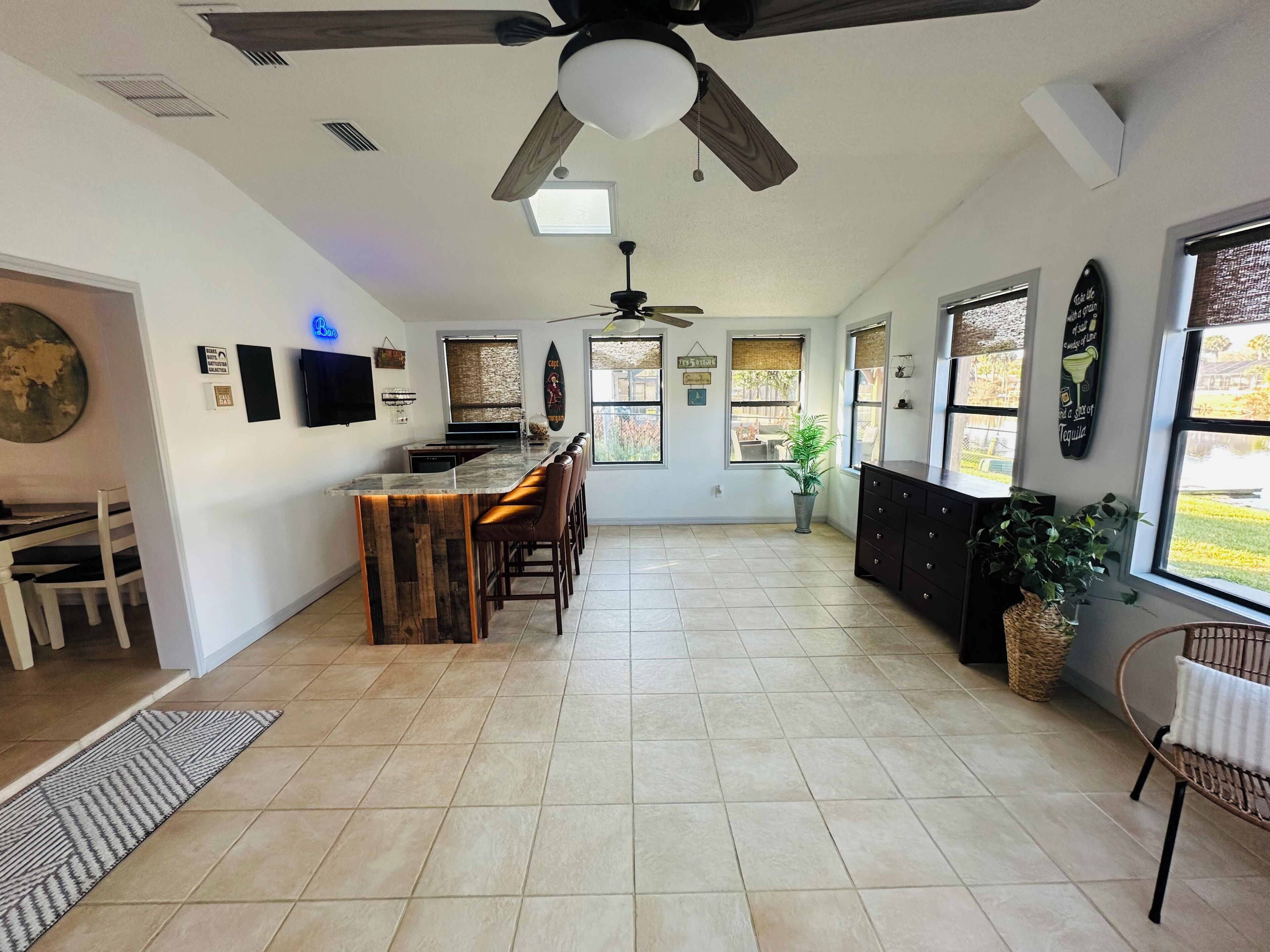 A spacious kitchen with a bar area, large windows, and a ceiling fan.