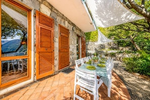 Un espace de restauration en plein air agrémenté d’un mur en pierre, de volets en bois et d’une table dressée pour deux personnes.