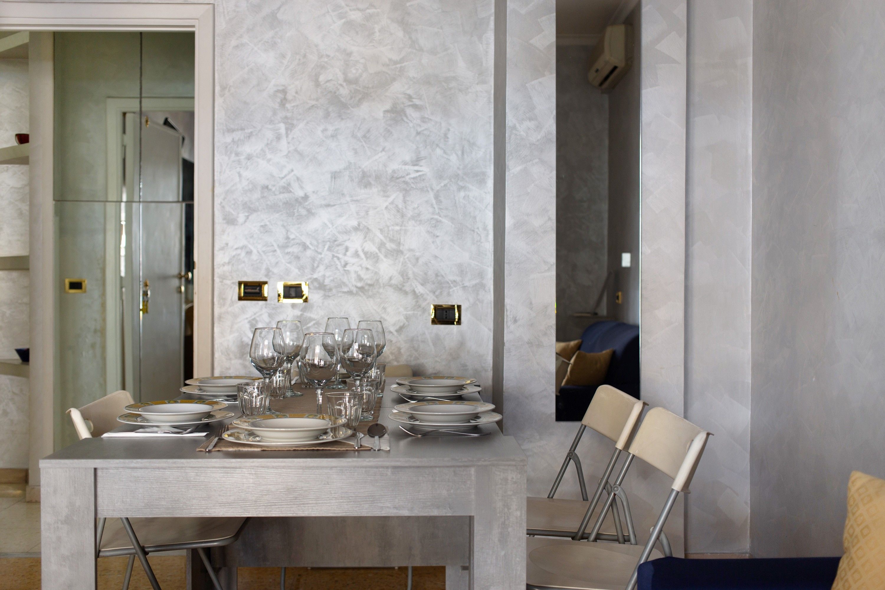 A dining area with a marble wall, a table set with plates and glasses, and a chair with a metal frame.
