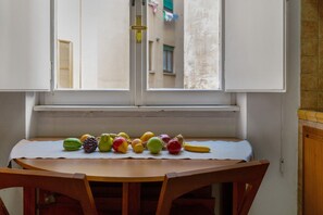 Eine Küche mit einem Fenster über einem Tisch, auf dem verschiedene Früchte präsentiert werden.