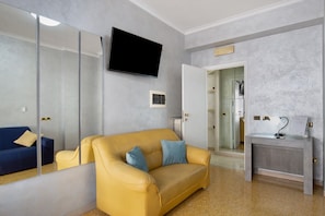 Ein modernes Hotelzimmer mit einer Couch, einem Fernseher, einem Schreibtisch mit Lampe und einem durchgegangenen Tür erkennbaren Badezimmer.