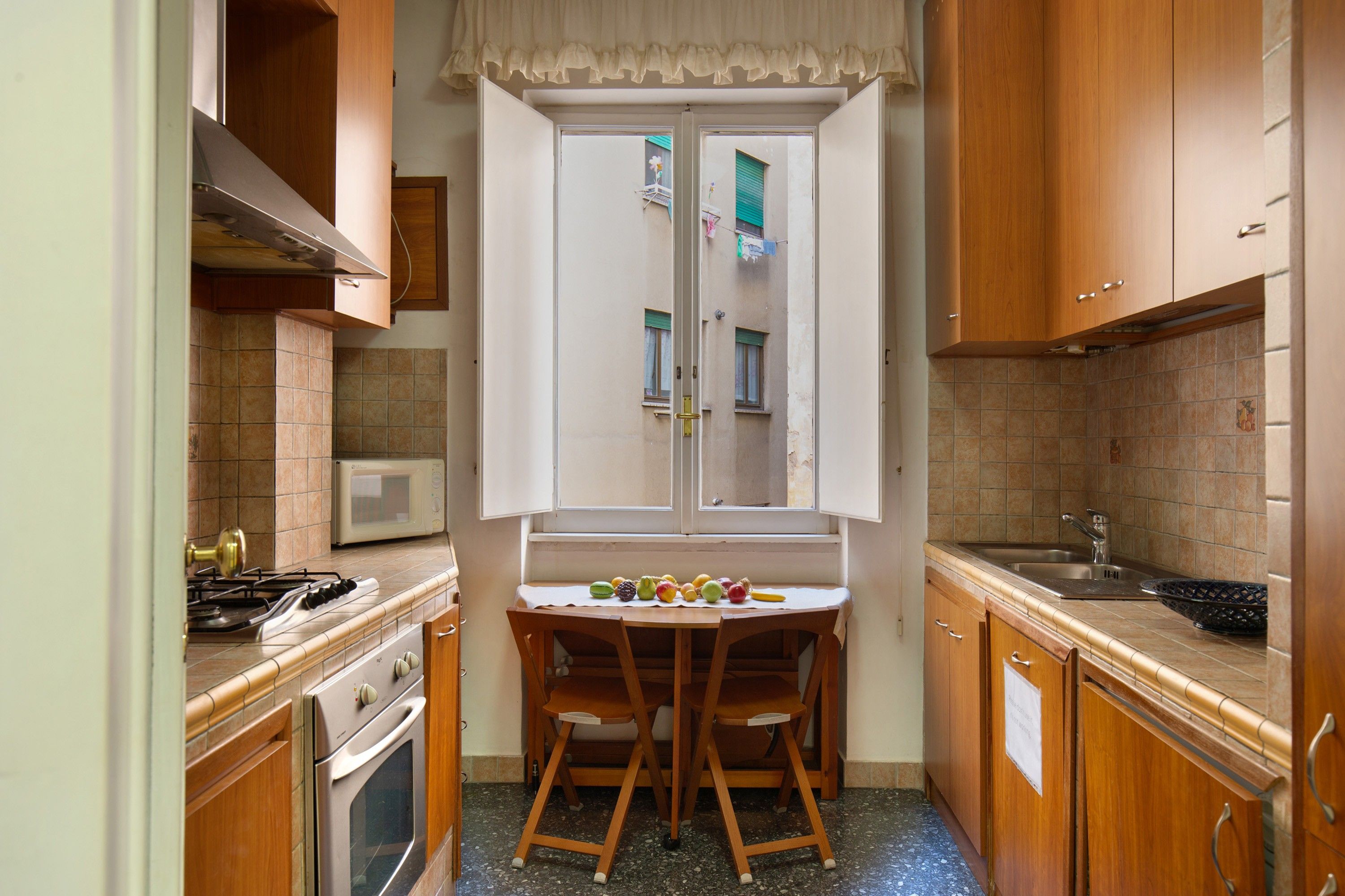 A compact kitchen with a stove, microwave, and a window with a view of a balcony.