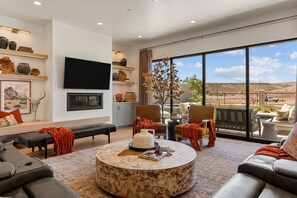 A modern living room with a large window, a flat-screen TV, and a fireplace. - Red Rock Isle: Private Pool + Hot Tub! Games! (Washington)