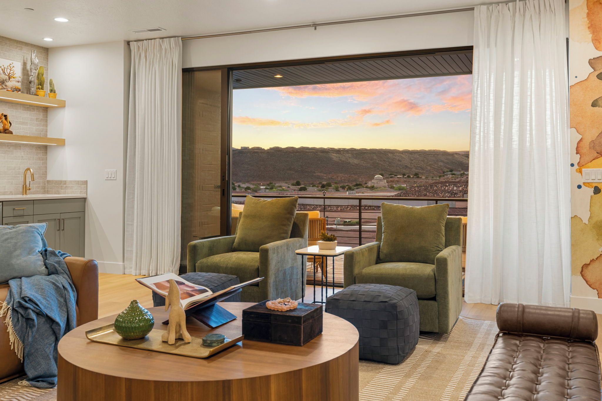 Un salon moderne doté d’une grande fenêtre offrant une vue panoramique, d’un coin salon confortable avec une table basse et d’une cuisine équipée d’un évier et agrémentée de plantes décoratives.