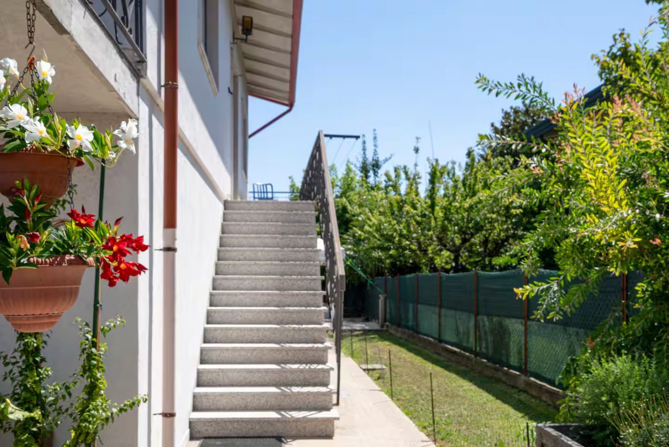 Un escalier menant à un bâtiment, entouré de verdure et d’une clôture.