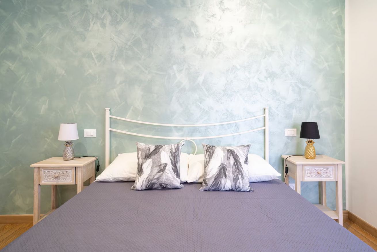 Un lit avec un cadre en métal blanc, deux tables de chevet avec des lampes et un mur à texture.