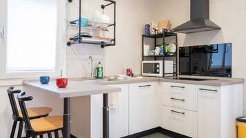Una cocina compacta con muebles blancos, una campana extractora negra, un microondas y un escurreplatos.