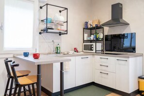 A compact kitchen with white cabinetry, a black range hood, a microwave, and a dish rack.