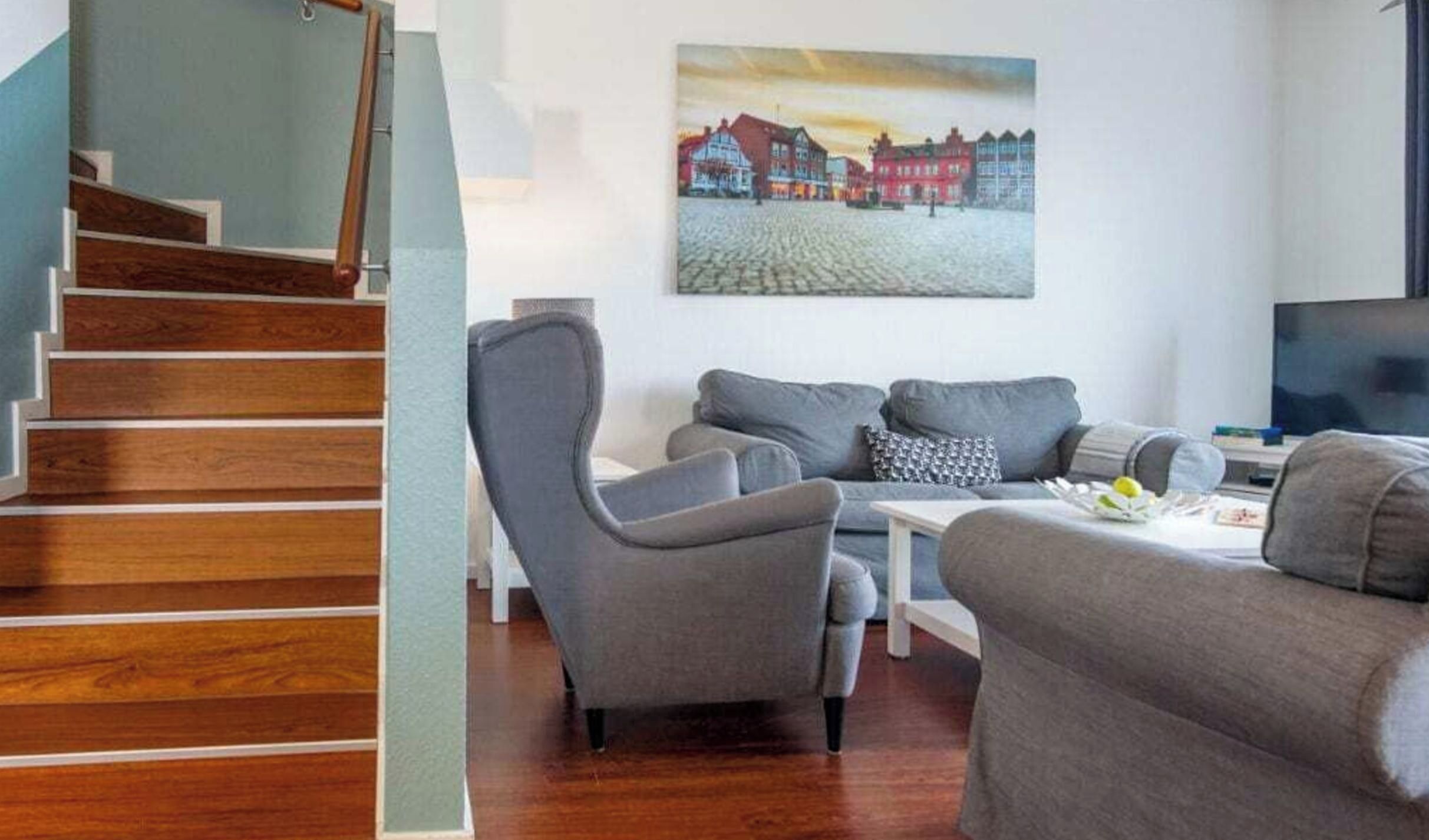 A living room with a grey sofa set, a coffee table, and a painting of a town scene on the wall.