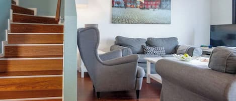 A living room with a grey sofa set, a coffee table, and a painting of a town scene on the wall.