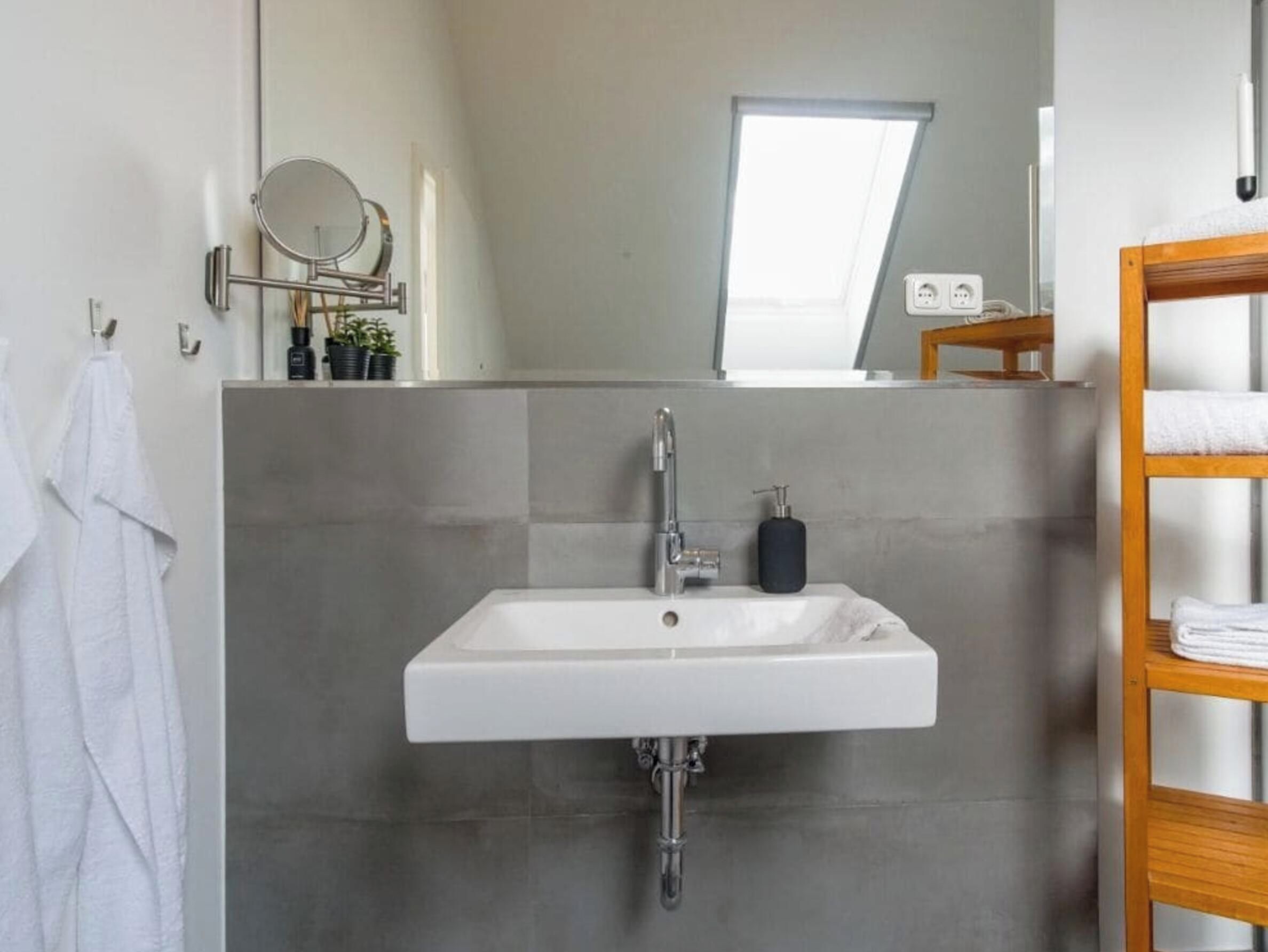 Ein Badezimmer mit einem weißen Waschbecken, einem Spiegel und einem Fenster.