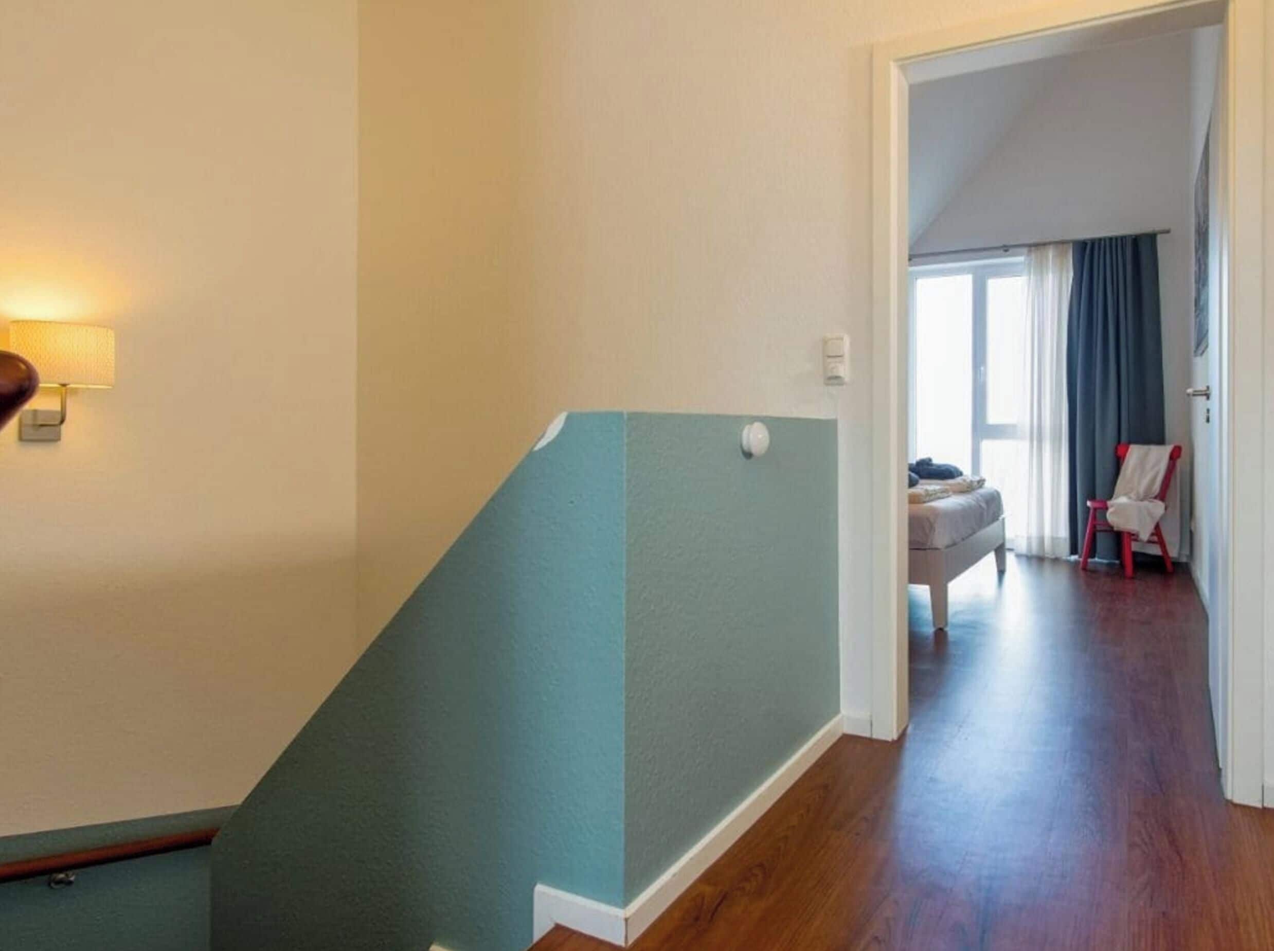 A staircase with a teal-colored handrail leading to a room with a bed and a chair.