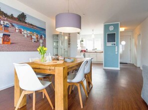 A dining area with a wooden table, white chairs, and a purple pendant light. - Holiday Home "luv" (Heiligenhafen)