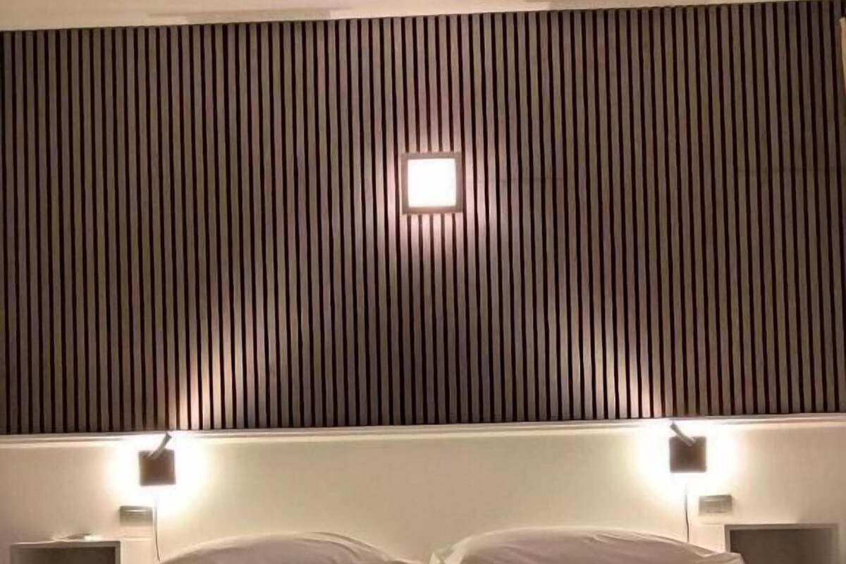 A hotel room with a bed, two bedside lamps, and a wall with vertical slats.