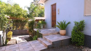 Propiedad residencial con entrada pavimentada, puerta de madera y un pequeño jardín con diversas plantas.