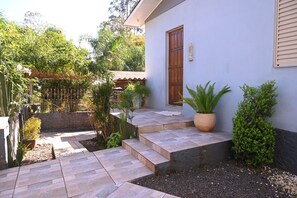 A residential property with a paved entrance, a wooden door, and a small garden area with various plants. - Casa com 3 Quartos Wi-fi e Quintal no Centro (Santa Rosa)