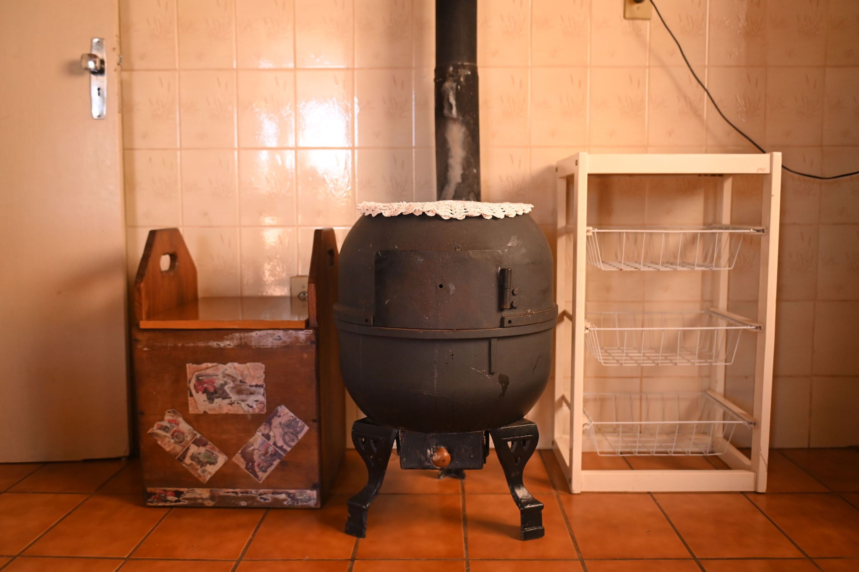 Uma cozinha com fogão preto grande, armário de madeira com fotos e estante de arame branca.