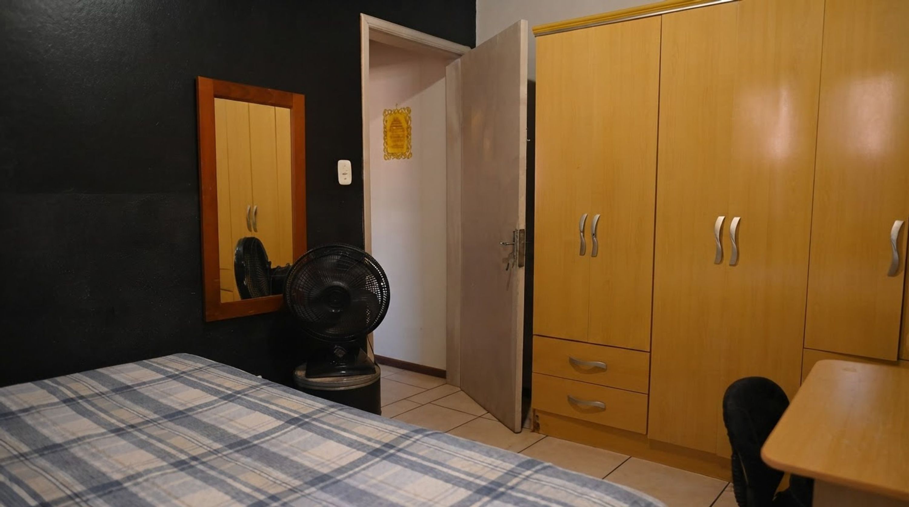 A bedroom with a bed, a fan, a wardrobe, and a small table.