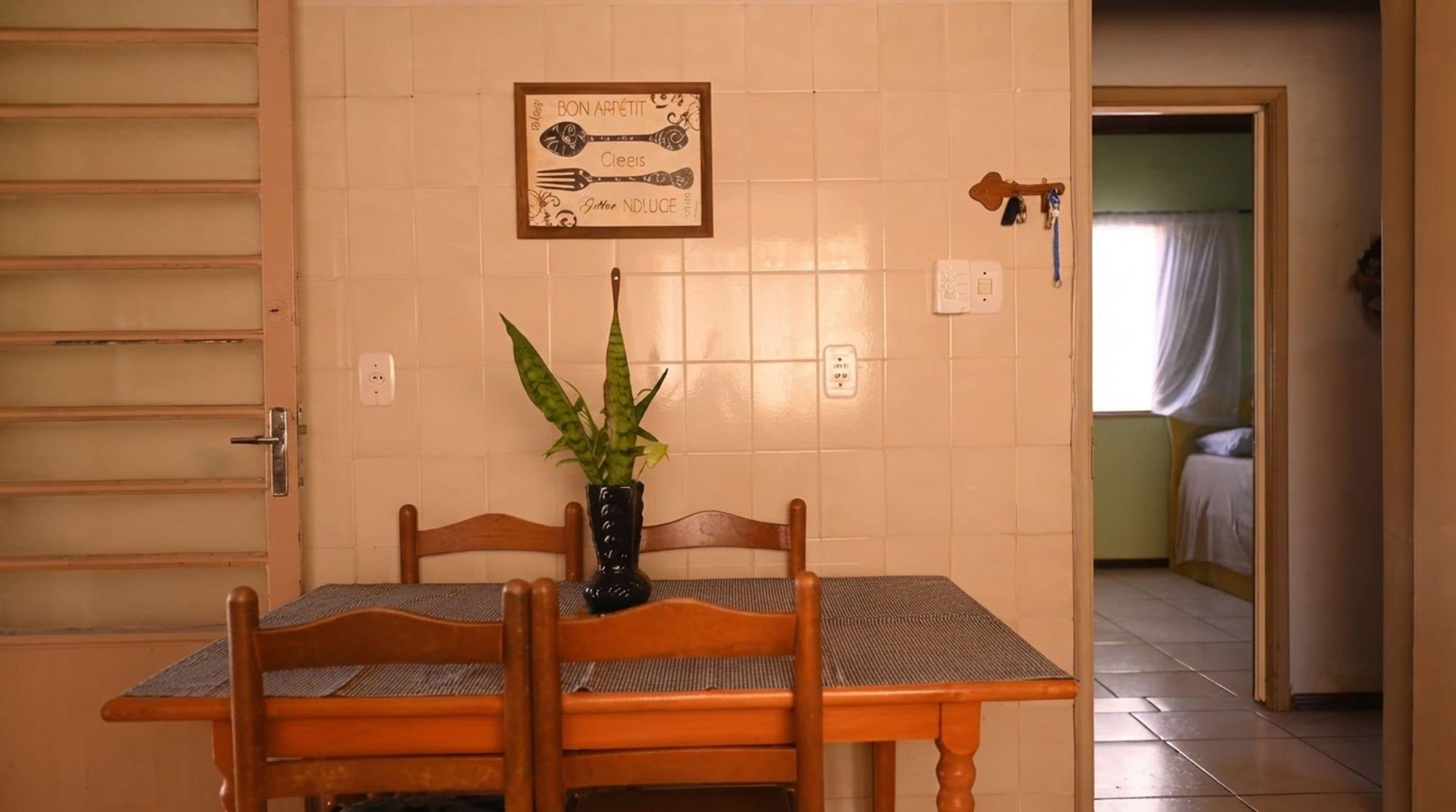 Uma área de refeições com mesa, cadeiras, uma planta em vaso e um letreiro fixado na parede.