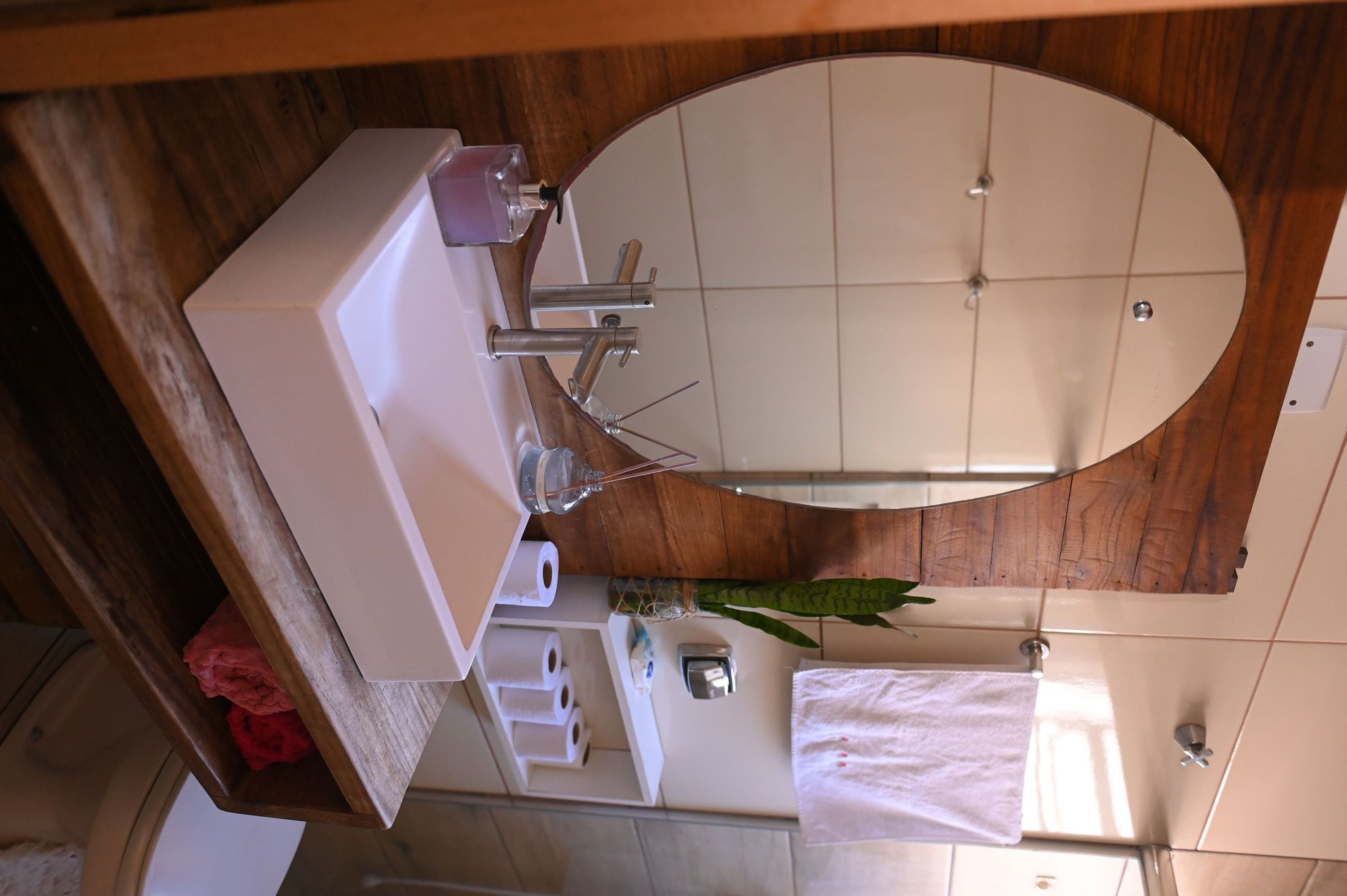 A bathroom with a wooden vanity, a round mirror, a white sink, and a towel hanging on the wall.
