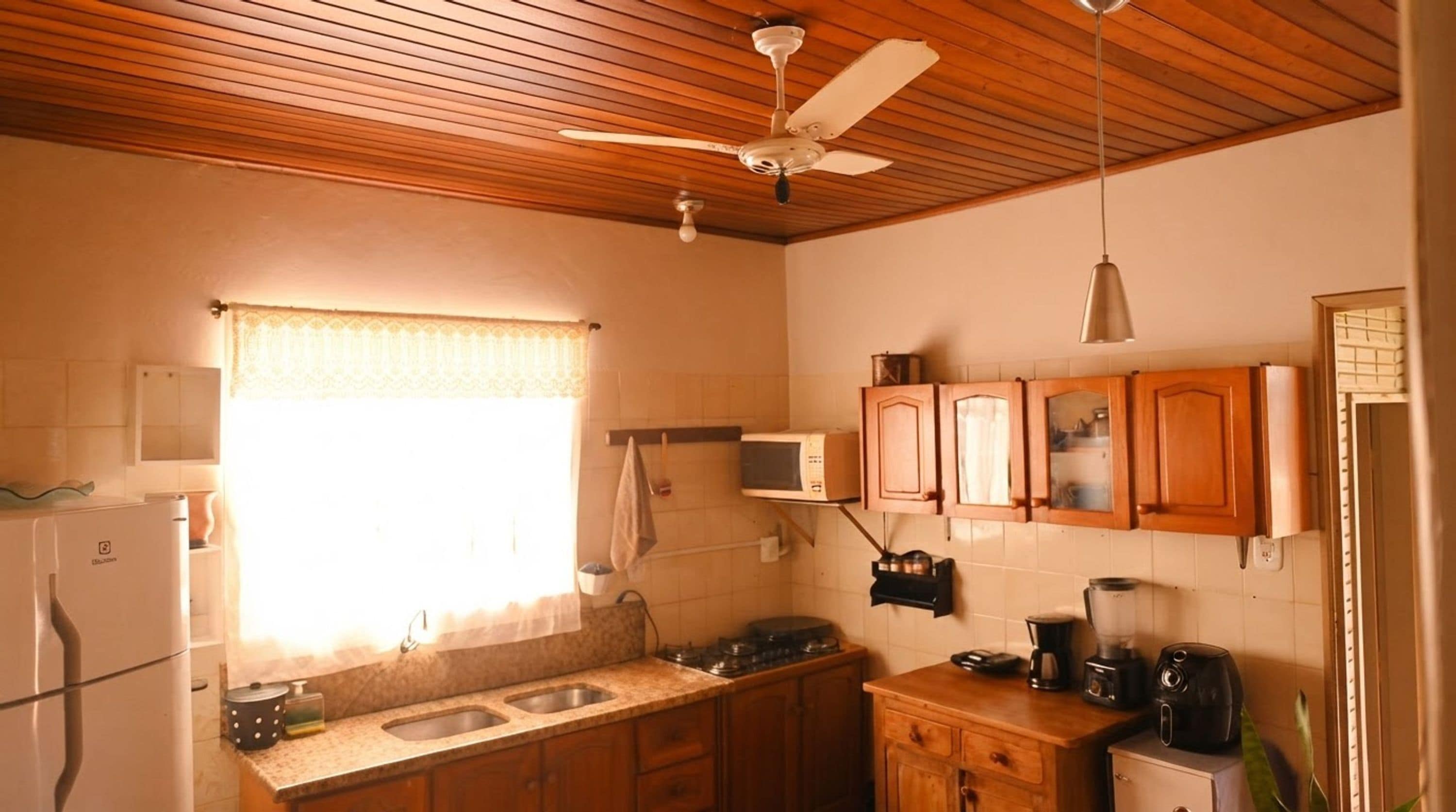 Cozinha compacta com armários de madeira, micro-ondas, fogão e ventoinha no teto.