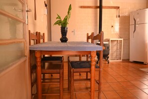 Un comedor con una mesa redonda, cuatro sillas de madera, mantel a cuadros y una planta en maceta.
