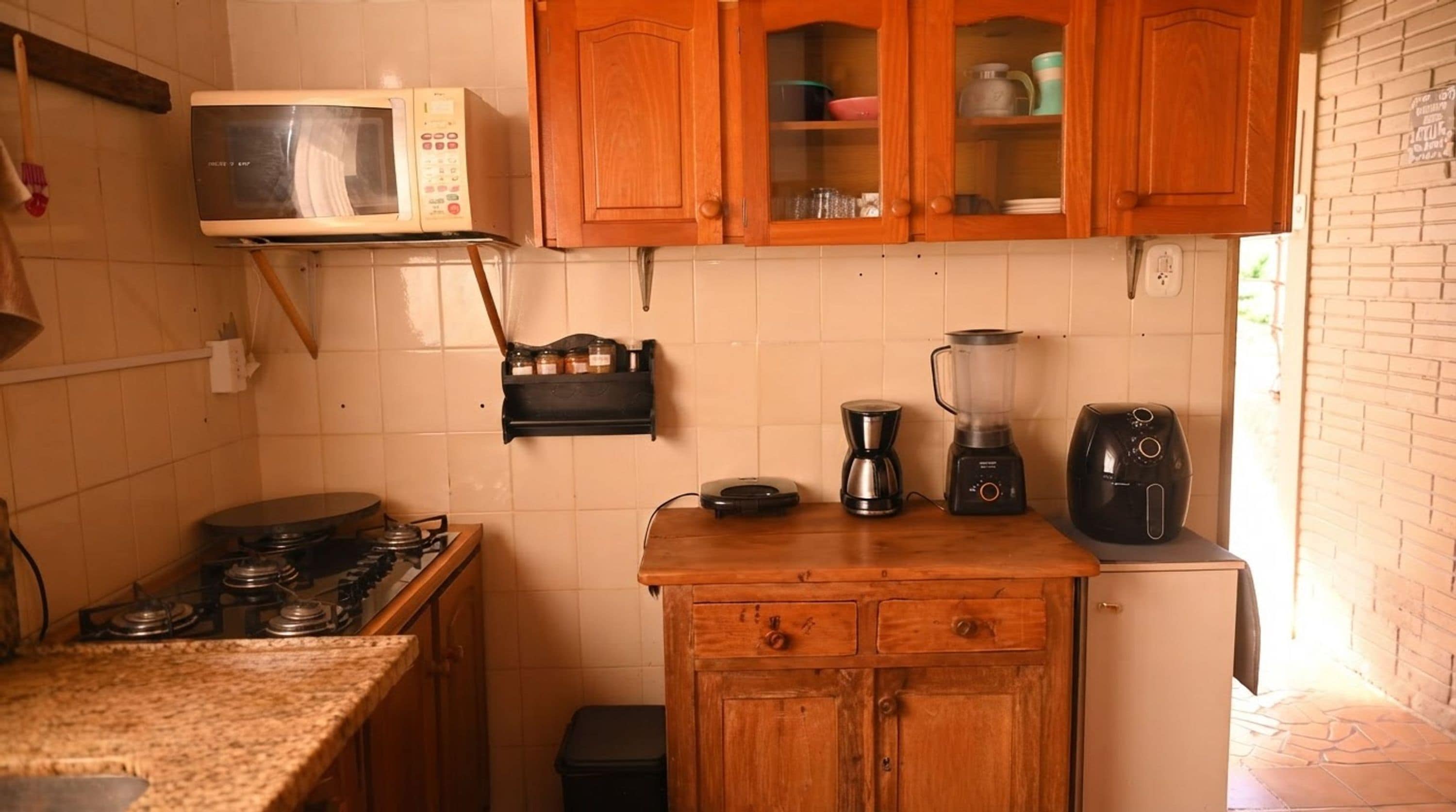 Cozinha compacta com fogão a gás, micro-ondas, liquidificador e armários de madeira.