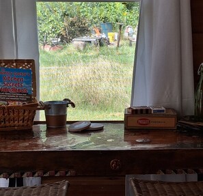 Ein Küchenfenster mit Blick auf ein Feld, ein Buch mit dem Titel 'The Country Doctor's Kitchen Secrets Handbook', ein Metalltopf und eine Packung 'PHILLIES PERFECTO' Zigaretten.