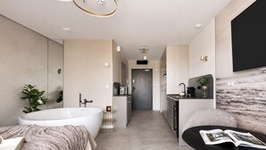 Een moderne badkamer met een ruime badkuip, een douche en een toilet. Er is een kleine keuken met een spoelbak en een koffieapparaat.