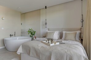 Een moderne slaapkamer met een groot bed, een badkuip en een nachtkastje met glazen en een dienblad.