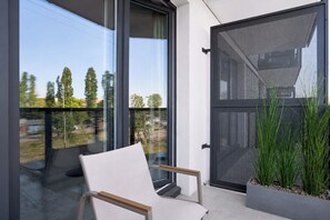 A modern balcony with a white chair, a glass door, and a view of trees and buildings. - Bubble Love Suites - Jacuzzi & Parking  (Gdańsk)