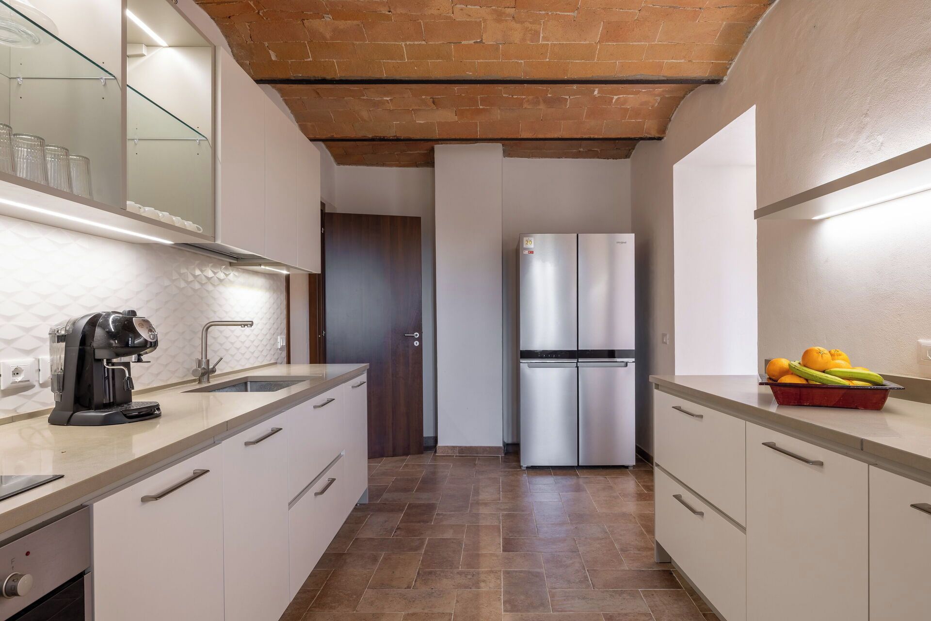 Una cocina moderna con armarios blancos, un refrigerador de acero inoxidable y una cafetera.