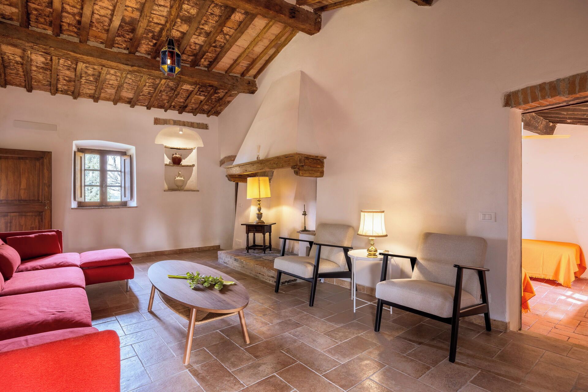 Un salon spacieux avec un haut plafond en bois, une cheminée, un ensemble de canapés rouges, une table basse ronde et deux fauteuils.