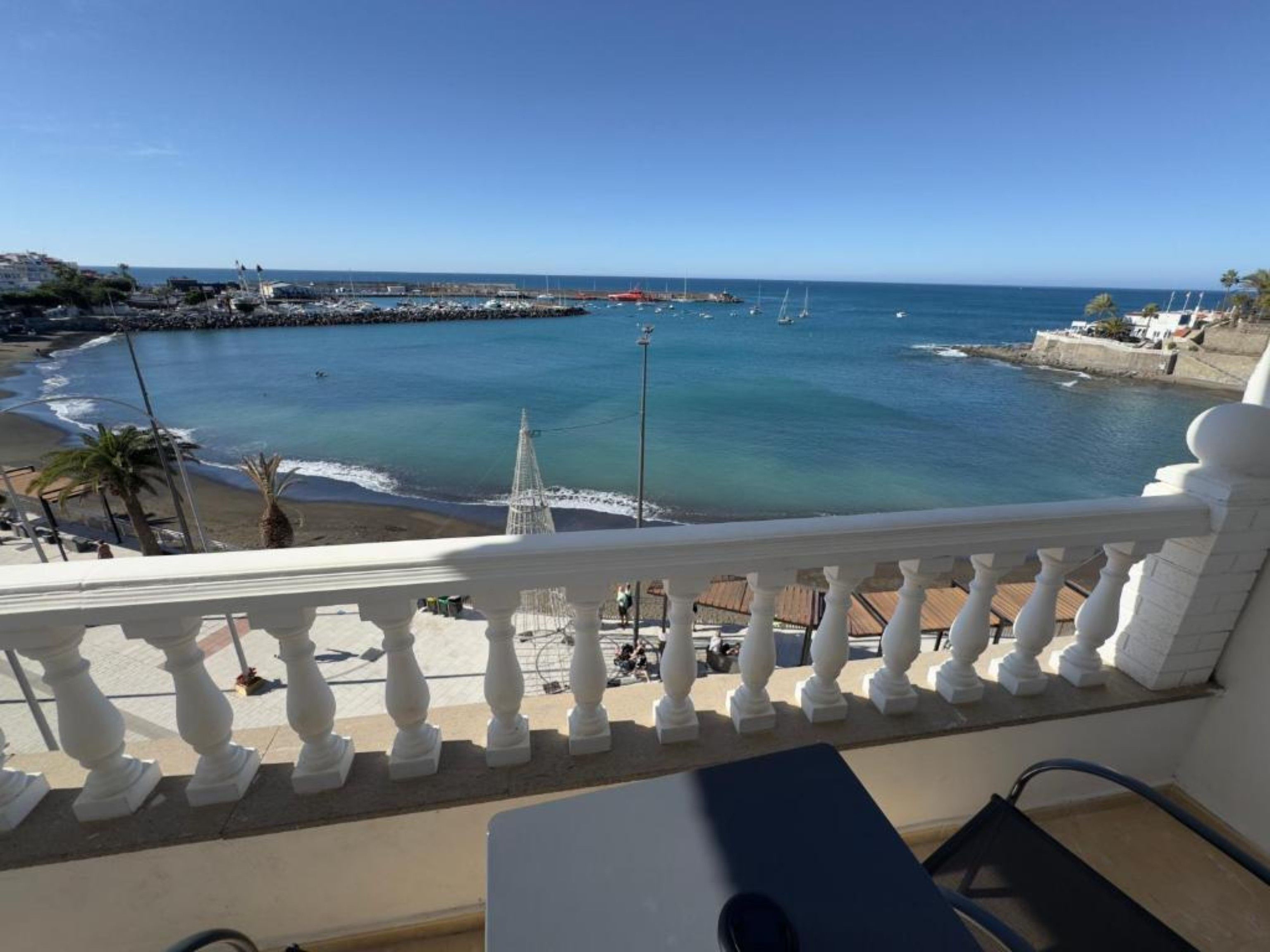 Een balkon met uitzicht op een kustgebied, inclusief een strand en een pier met boten.