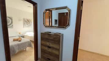 Een kamer met een houten dressoir, een spiegel en een bed met een grijze deken.