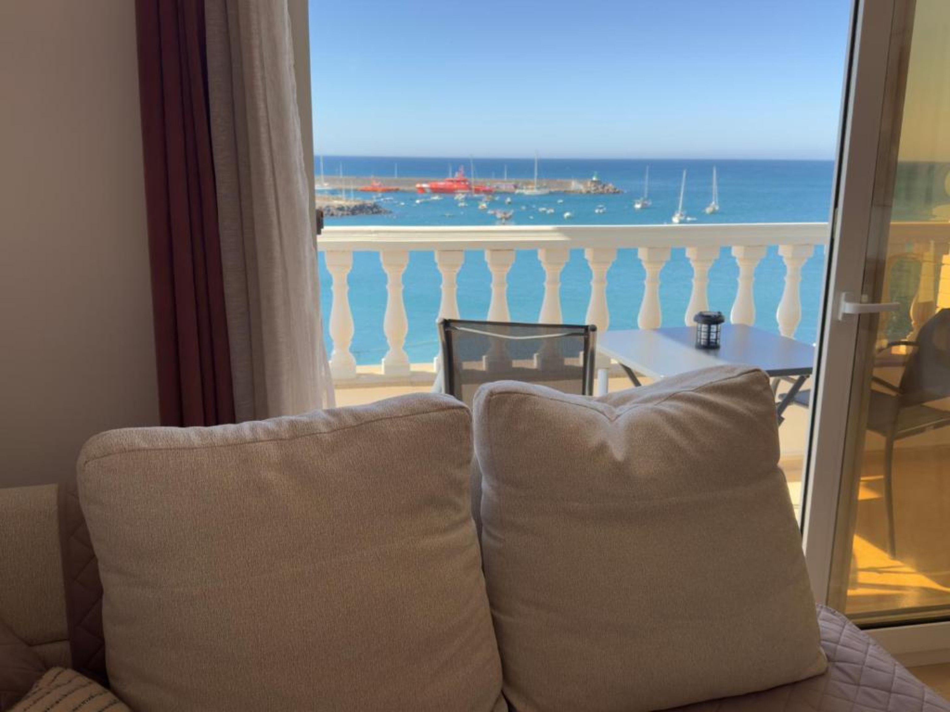 A balcony with a view of the sea, a table, and chairs.