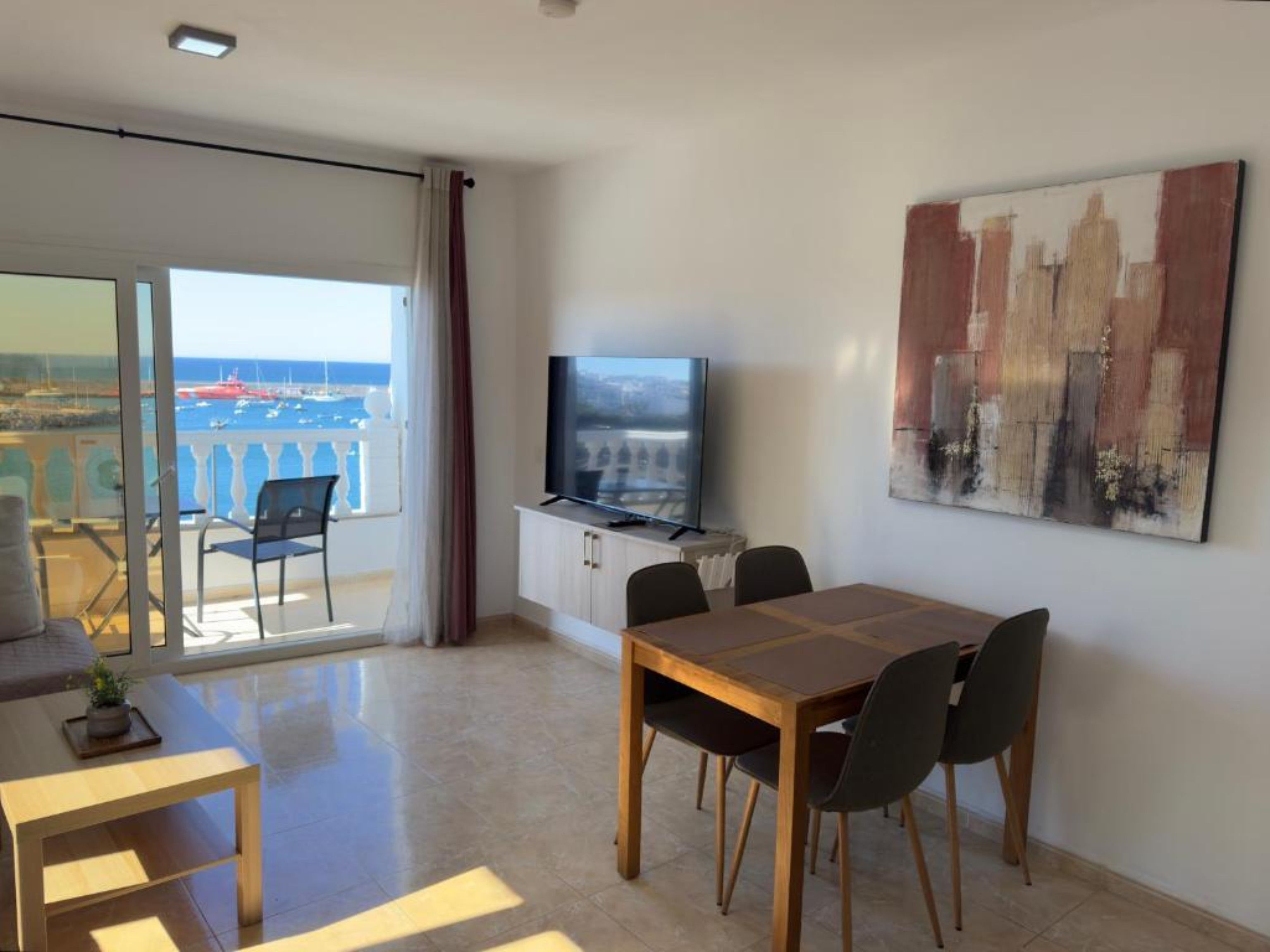 Une chambre d’hôtel avec un balcon, une table à manger avec des chaises, un téléviseur et un tableau au mur.