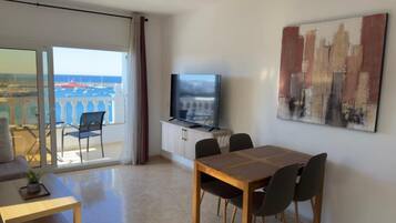 Une chambre d’hôtel avec un balcon, une table à manger avec des chaises, un téléviseur et un tableau au mur.