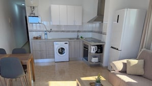 A compact living space with a kitchenette, a washing machine, a dining area with a table and chairs, and a sofa.
