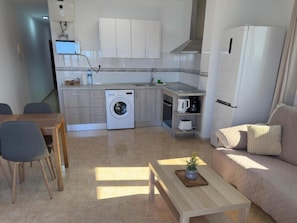 A compact living space with a kitchenette, a washing machine, a dining area with a table and chairs, and a sofa.