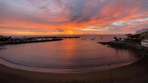 Atardecer costero con barcos, mar en calma y edificios a lo largo de la costa.