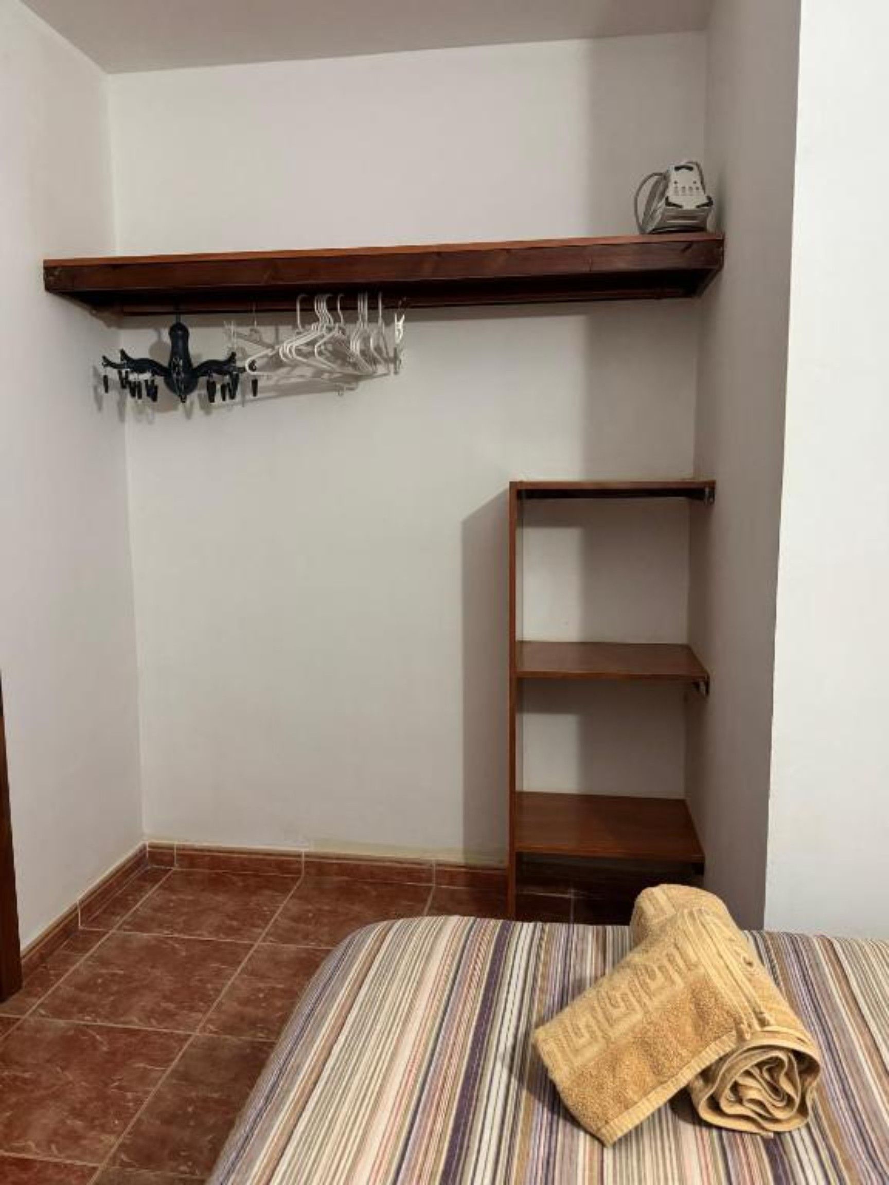 Ein kleines Zimmer mit einem Bett, einem Holzregal und einem Kleiderständer.