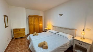 Une chambre à coucher avec un lit double, une armoire en bois, une table de chevet avec une lampe et une petite commode.